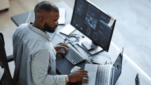 Um profissional focado em desenvolvimento de software e análise de dados trabalha em um ambiente com várias telas de computador, aplicando conceitos de CMMI e Agile.